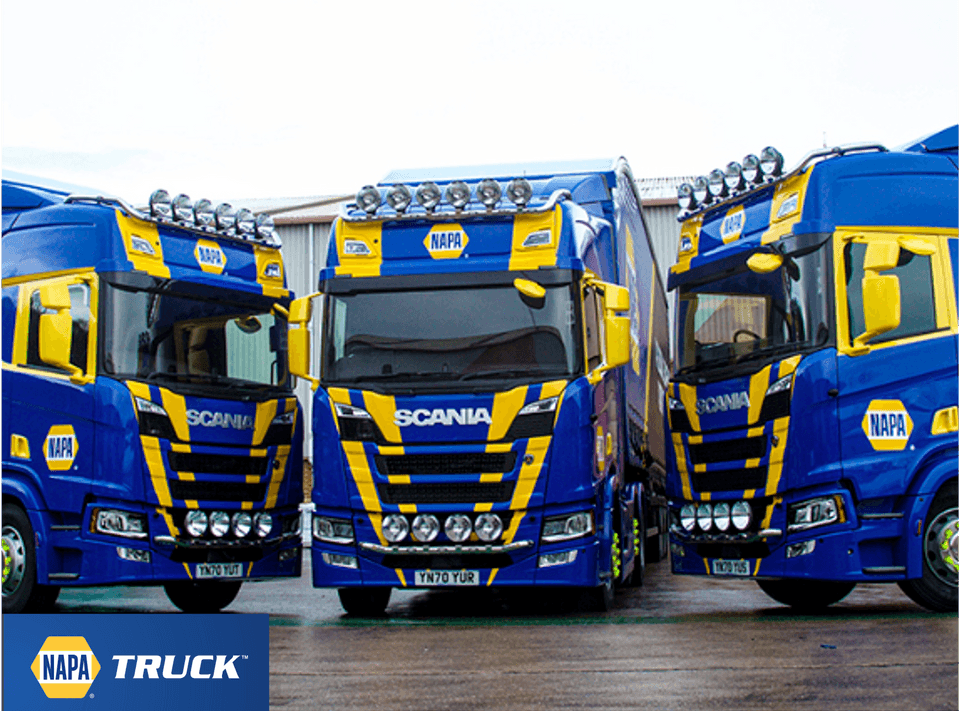 Three blue and yellow truck lined up on a forecourt